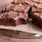 butternut squash brownies on a parchment lined wire cooling rack topped with chocoalte avocado frosting, one brownie with a bite taken out of it
