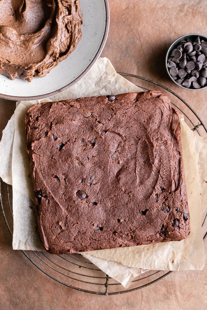 baked 8x8 butternut squash brownies unfrosted with a bowl of chocolate avocado frosting above it