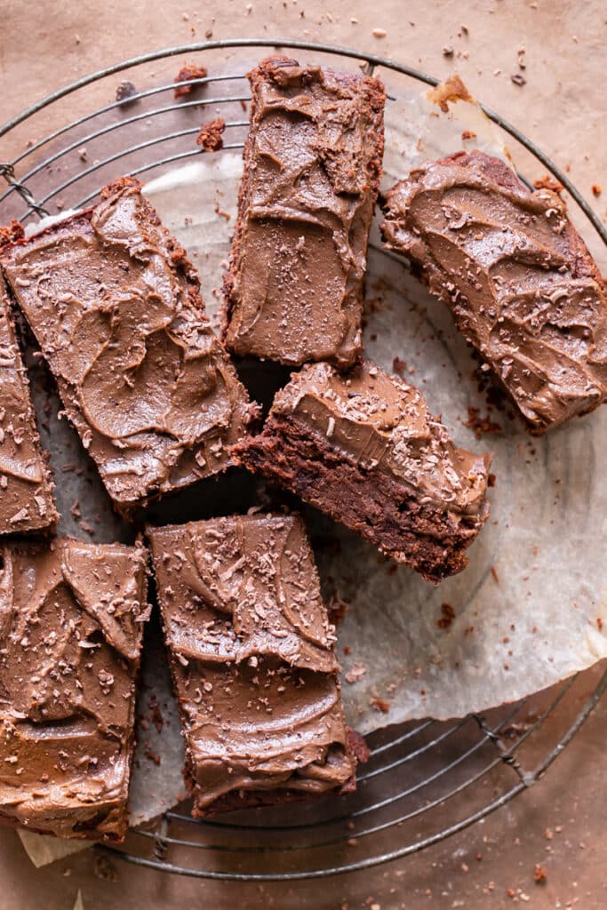 butternut squash brownies frosted with chocolate avocado frosting laid out on a parchment lined wire cooling rack sliced into bars