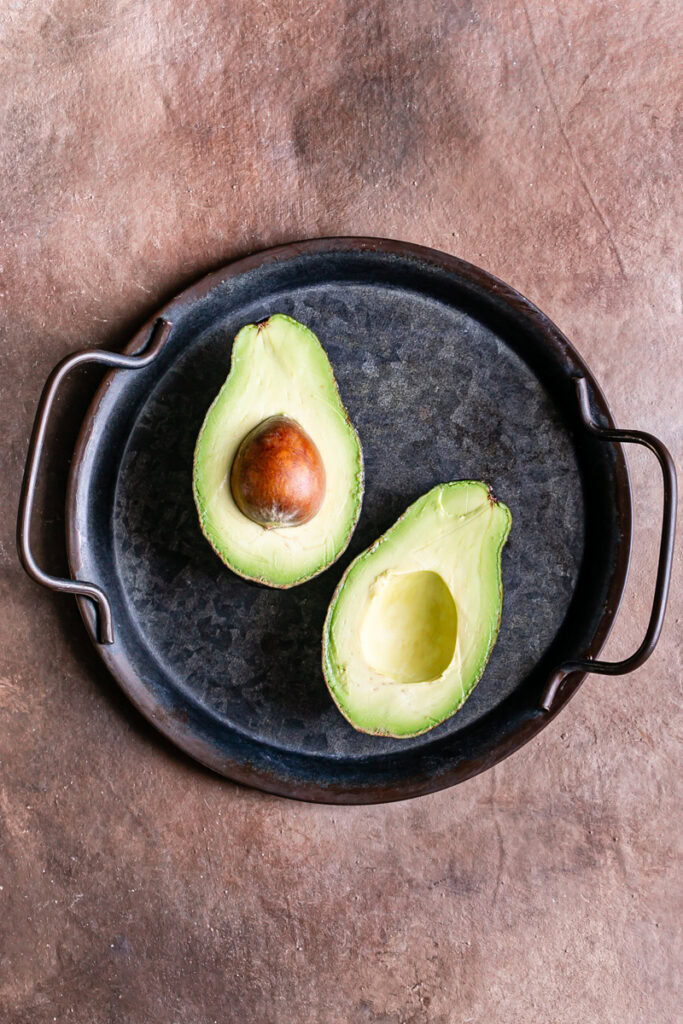 an avocado sliced in half revealing the green flesh and pit of the avocado
