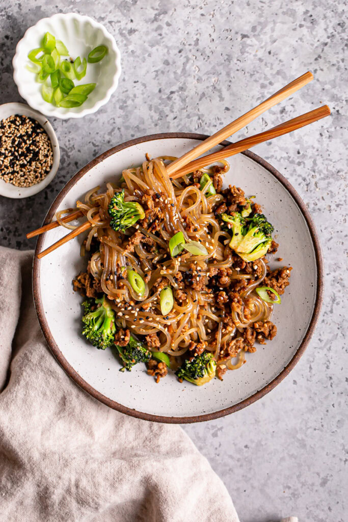 a close up of one bowl of vegan beef and broccoli teriyaki noodles with noodles twirled around the chopsticks