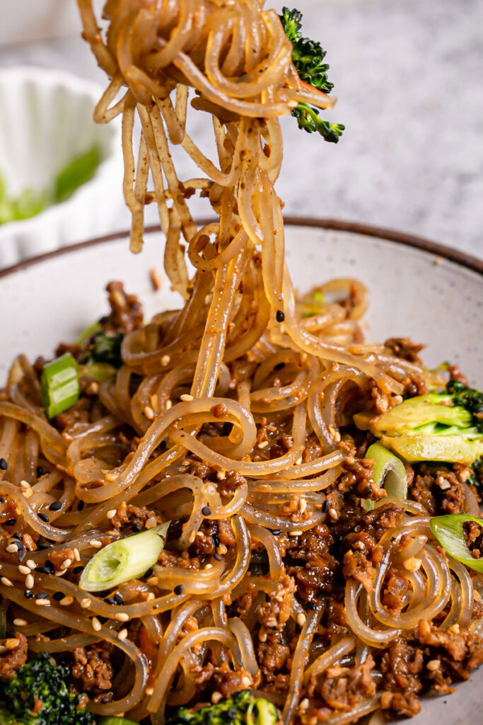a very close up image of pulling some of the gluten-free glass noodles out of the bowl with chopsticks