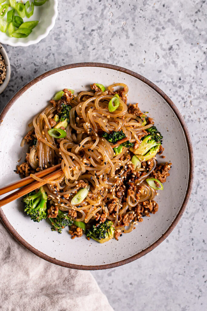 a close up of one bowl of vegan beef and broccoli teriyaki noodles with noodles twirled around the chopsticks