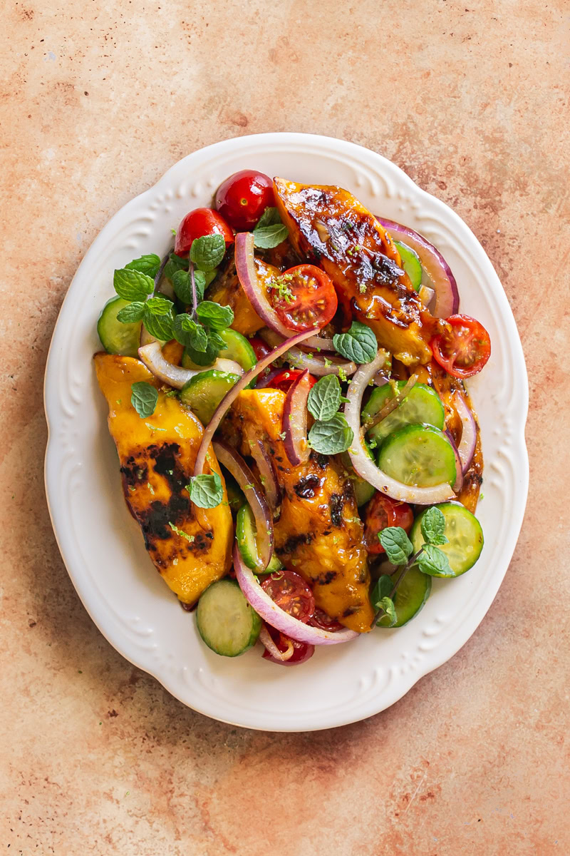 grilled mango sweet chili lime salad on a white scalloped plate garnished with fresh mint