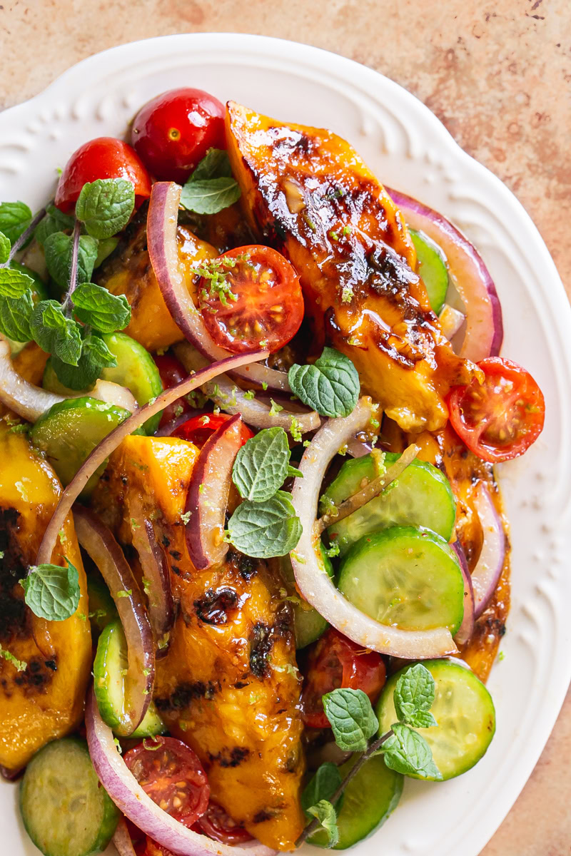 close up of grilled mango sweet chili lime salad on a white scalloped plate garnished with fresh mint