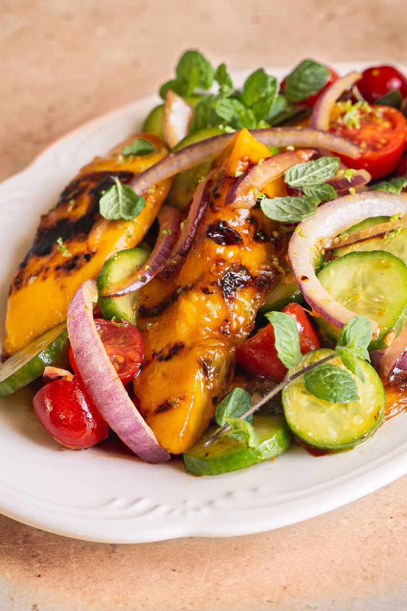 3/4 close up shot of grilled mango sweet chili lime salad on a white scalloped plate garnished with fresh mint