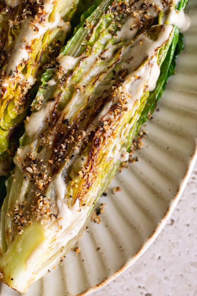 a close up of one of the halves of grilled romaine lettuce drizzled with caesar dressing and toasted breadcrumbs