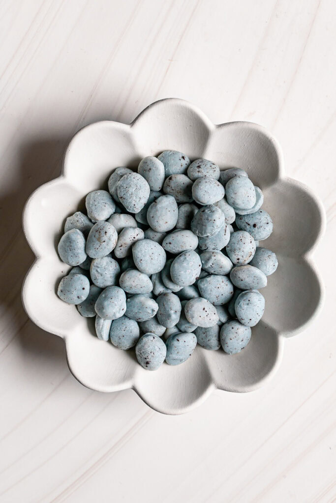 a flower shaped bowl filled with the robin's egg white chocolate covered almonds.
