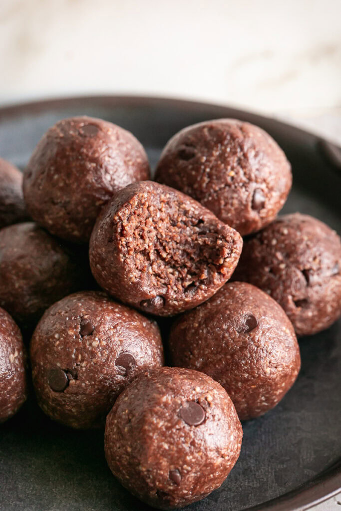 a close up of Sunflower seed chocolate brownie bites rolled and stacked on a round metal plate, the top bite with a bite taken out of it.