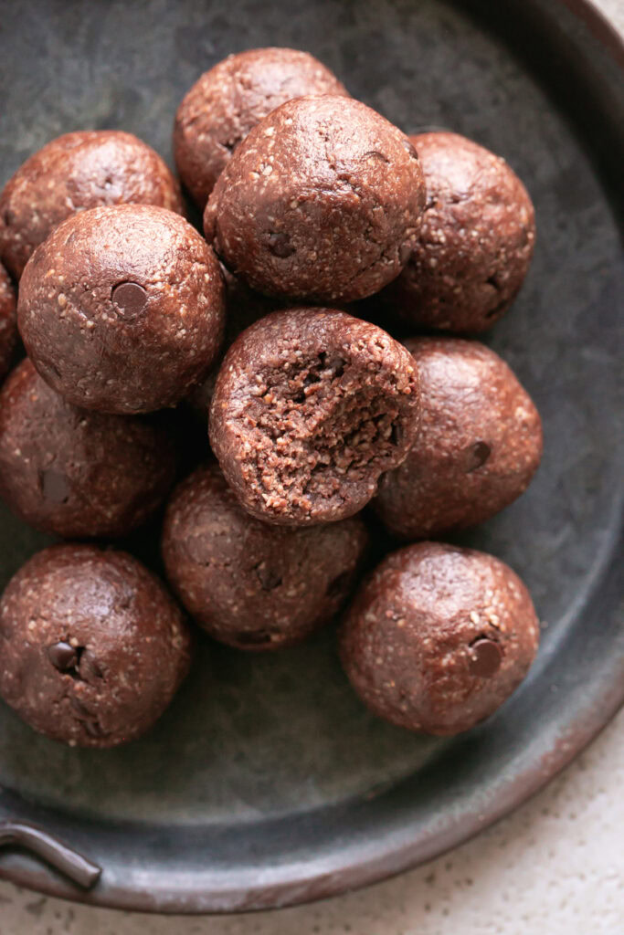 an overhead shot of Sunflower seed chocolate brownies bites rolled and stacked on a round metal plate, the top bite with a bite taken out of it.
