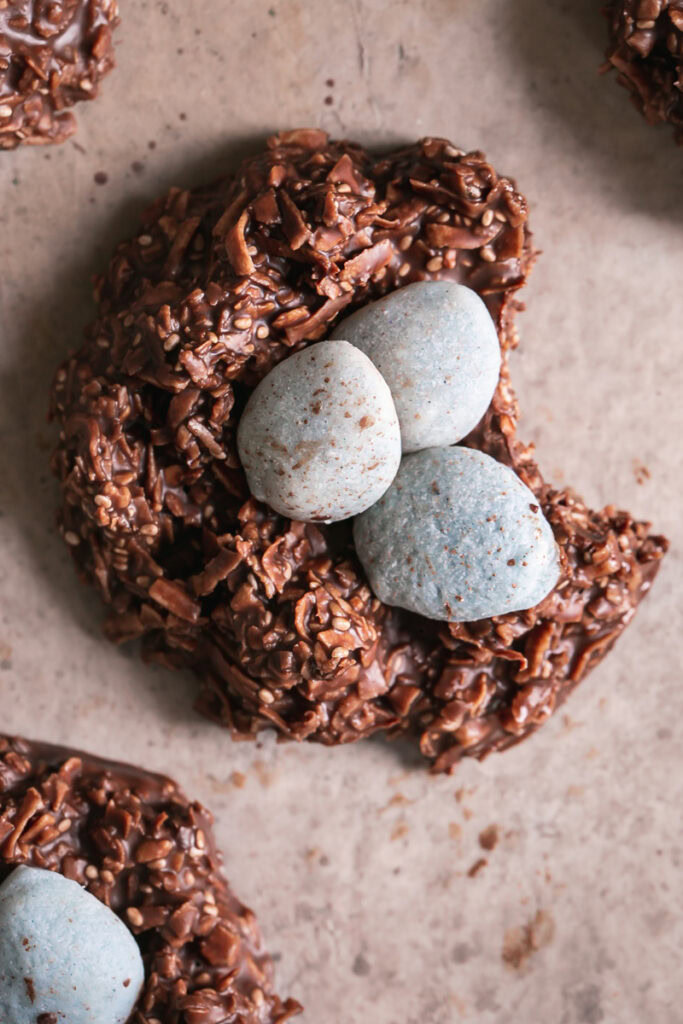 a close up of one Toasted Coconut Chocolate Bird's Egg Nest Cookie filled with three robin's egg white chocolate covered almonds with a bite taken out of the cookie