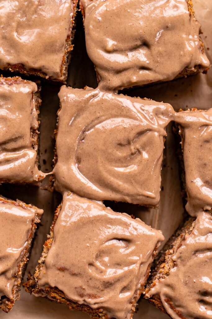 a close up of maple tahini banana bread bars iced with a maple tahini protein frosting sliced into squares and spread out on a piece of parchment paper