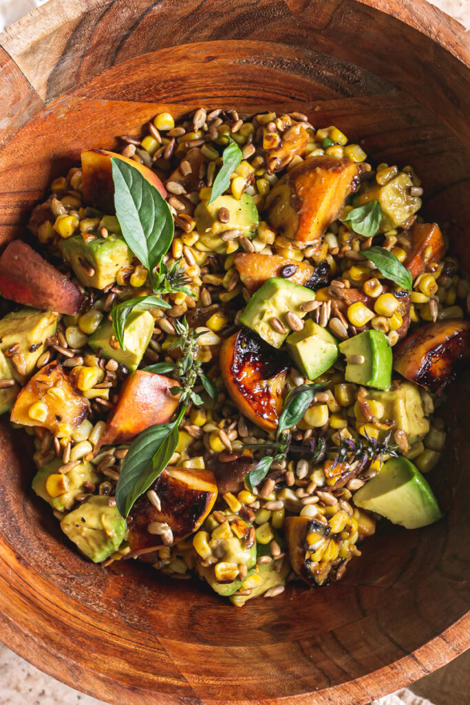 close up shot of Grilled Corn Peach Avocado Salad with Orange Ginger Miso Dressing in a wooden bowl