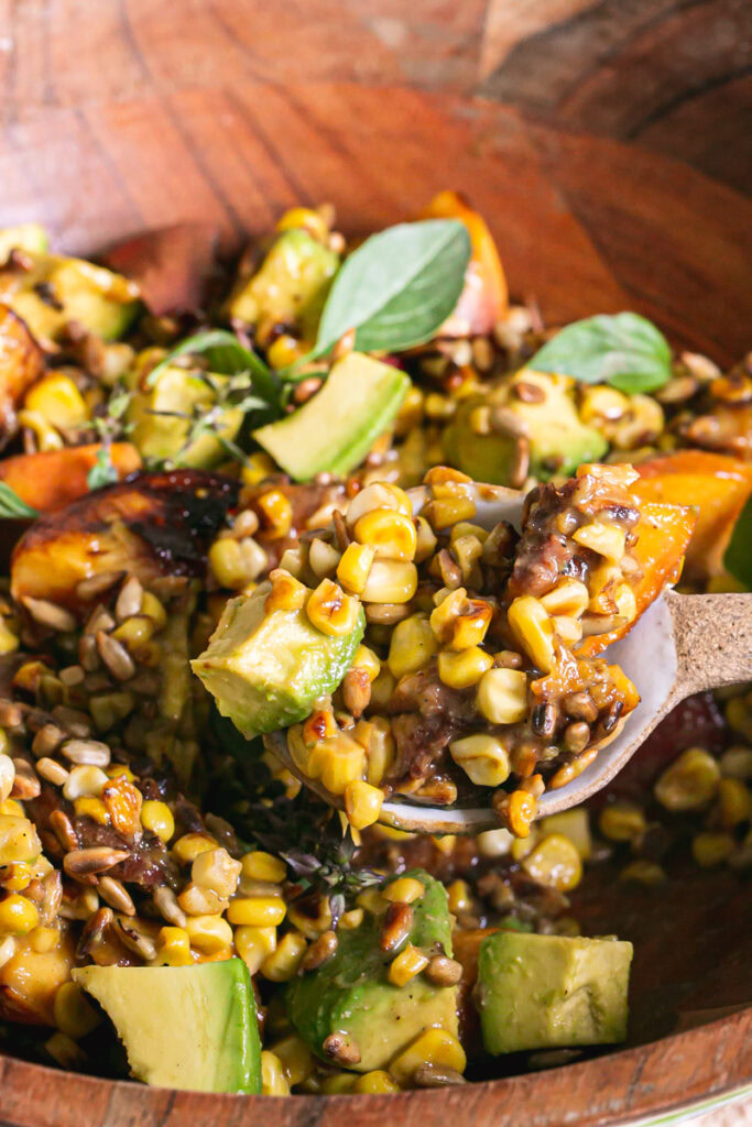 a close up of spooning some of the Grilled Corn Peach Avocado Salad with Orange Ginger Miso Dressing out of the wooden bowl