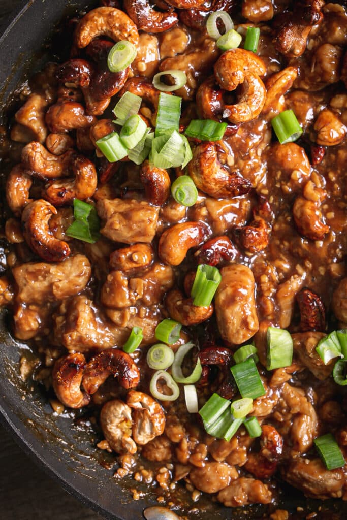 cooked vegan sticky cashew chicken in a skillet garnished with sliced green onions