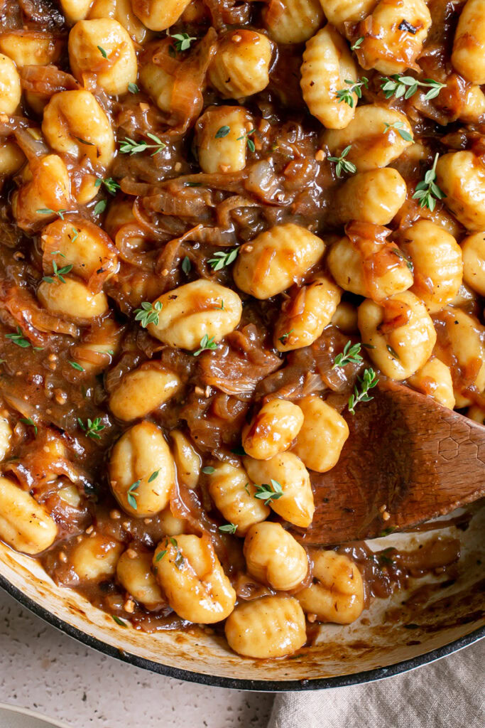 French Onion Gnocchi in a large skillet with a wooden spoon in the skillet