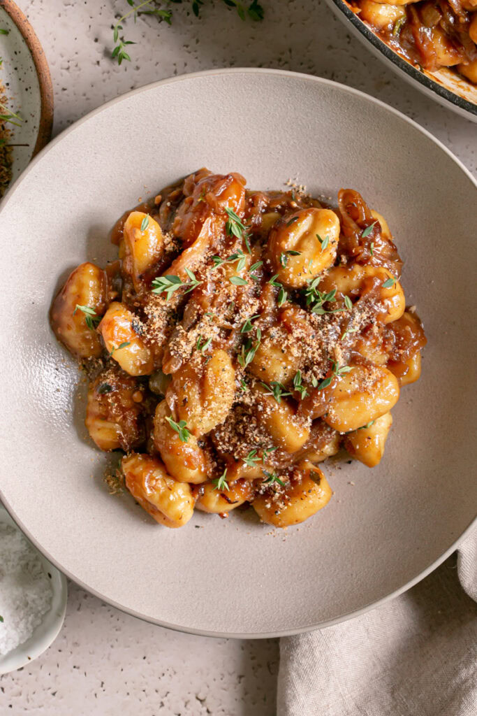 a close up of a bowl of French Onion Gnocchi garnished with fresh thyme leaves and toasted breadcrumbs