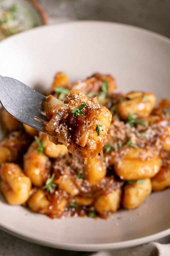 close up of French onion gnocchi on a fork with the rest of the gnocchi out of focus in a bowl in the background