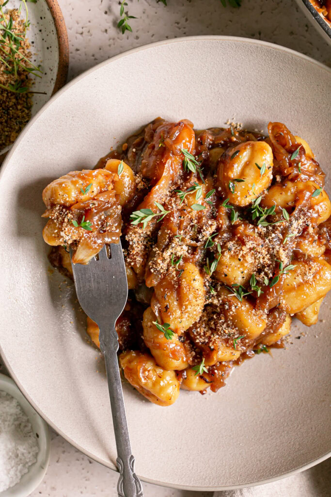 close up of French Onion Gnocchi in a bowl garnished with fresh thyme leaves and toasted breadcrumbs, gnocchi on a fork in the bowl