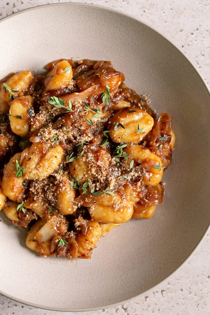 close up of French Onion Gnocchi in a bowl garnished with fresh thyme leaves and toasted breadcrumbs