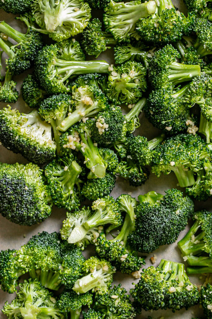 raw broccoli florets tossed in avocado oil and minced garlic on a parchment lined baking sheet