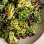 a closeup of a bowl of broccoli tossed with fresh dill and raisins and a harissa tahini dressing