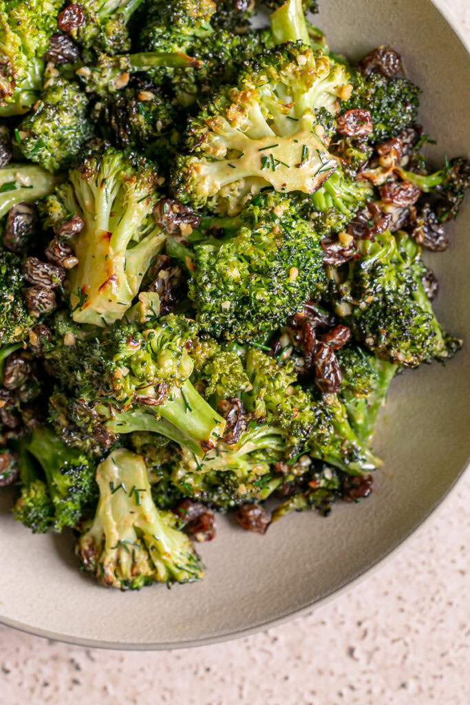 a closeup of a bowl of broccoli tossed with fresh dill and raisins and a harissa tahini dressing