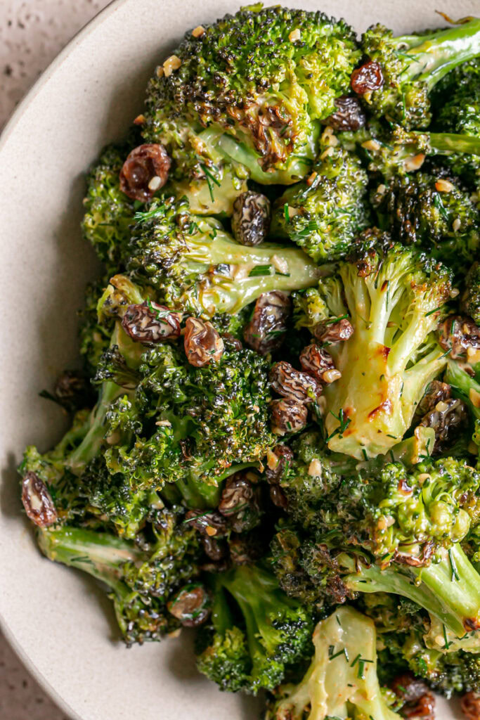 a closeup of a bowl of broccoli tossed with fresh dill and raisins and a harissa tahini dressing