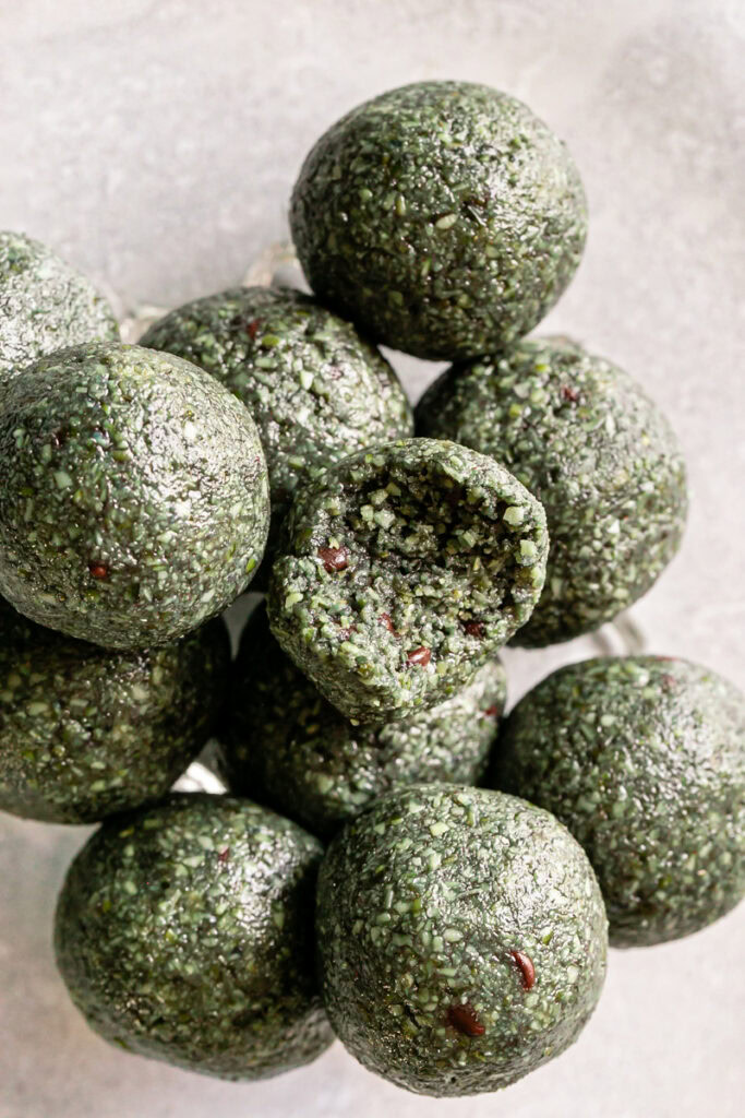 overhead shot of Spirulina Pumpkin Seed Chocolate Chip Bites stacked on top of one another, one with a bite taken out of it