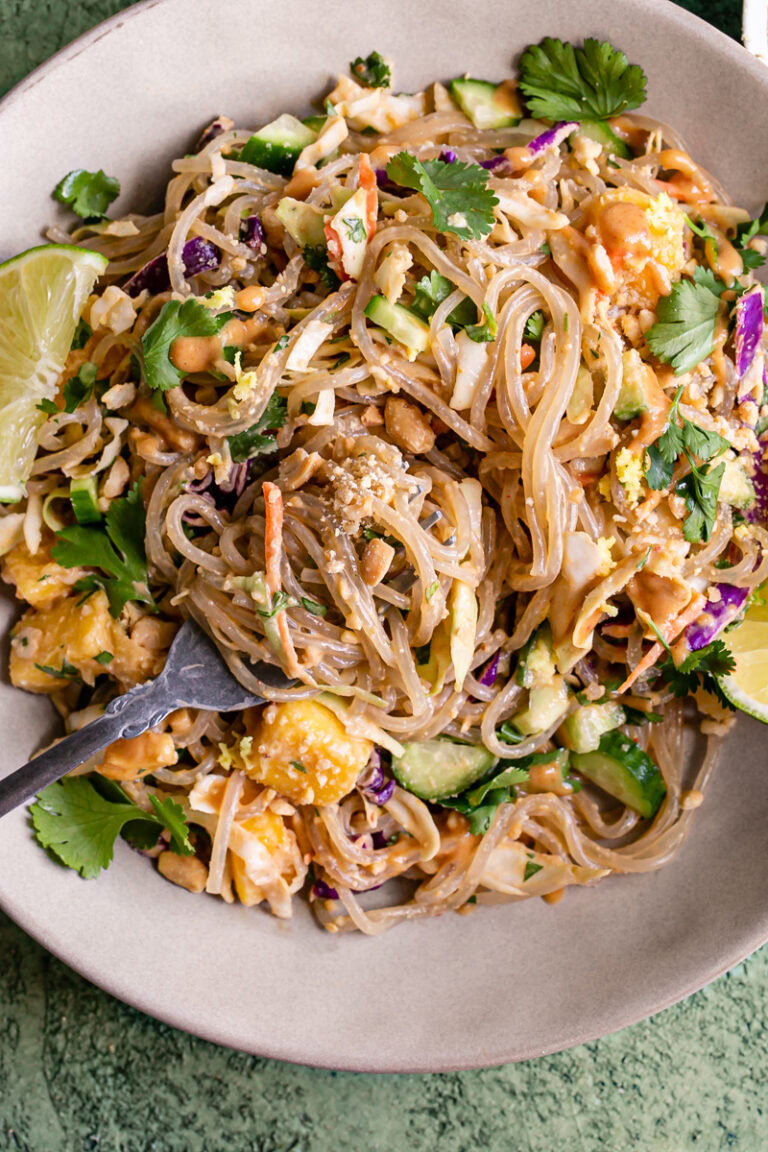a very close up image of Thai Peanut Glass Noodle Salad in a bowl with a lime wedge and a fork in the bowl with noodles spun around it