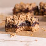 a single Peanut Butter Oat Date Crumb Bar with a bite taken out of it on a piece of parchment paper with more bars behind it