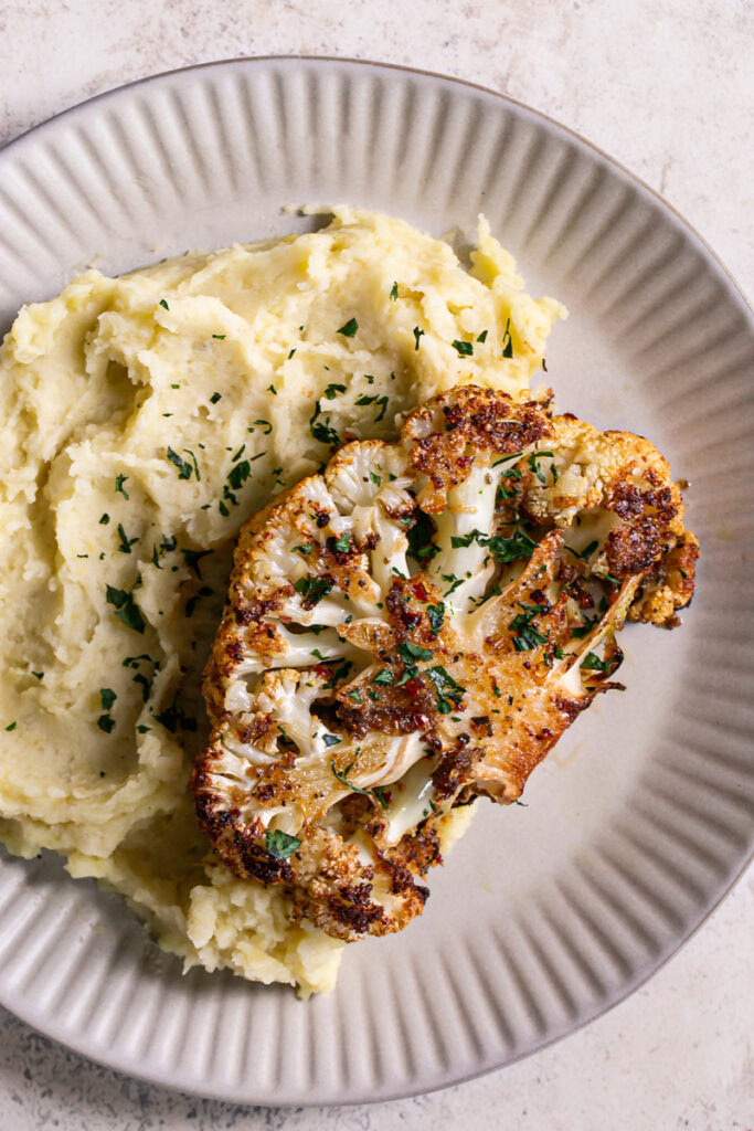 a dinner plate with mashed potatoes and Kick'n Chick'n Roasted Cauliflower Steak on top garnished with fresh parsley