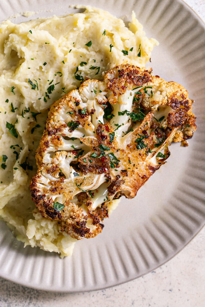 a dinner plate with mashed potatoes and Kick'n Chick'n Roasted Cauliflower Steak on top garnished with fresh parsley