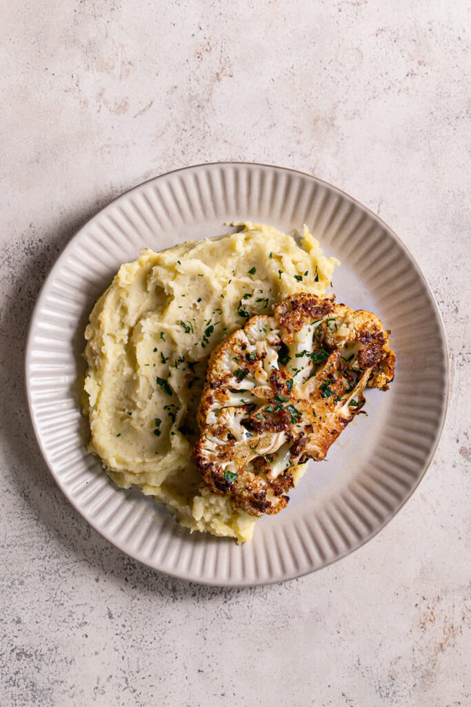 a dinner plate with mashed potatoes and Kick'n Chick'n Roasted Cauliflower Steak on top garnished with fresh parsley