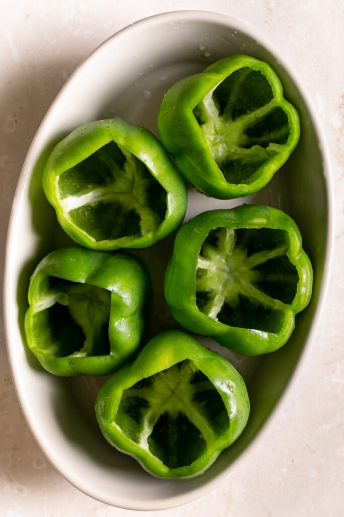 5 hollowed out green bell peppers in an oval baking dish