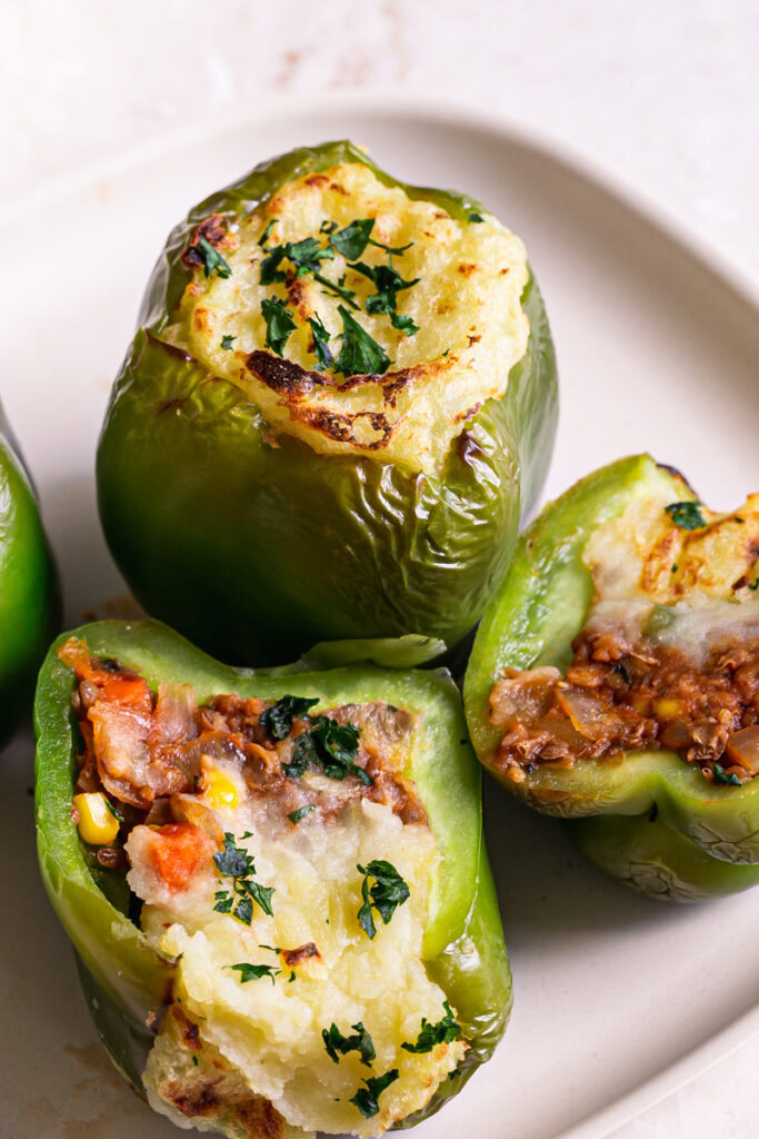 shepherd's pie stuffed peppers on a plate, one pepper cut in half to reveal the filling