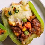a shepherd's pie stuffed green bell pepper cut in half to reveal the lentil shepherd's pie filling topped with mashed potatoes