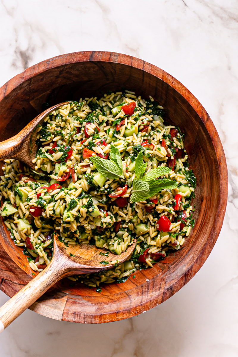 gluten-free Tabouli Orzo Salad garnished with fresh mint leaves in a wooden bowl with a wooden salad servers in the bowl