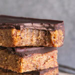 a close up of three almond flour date cookie dough bars stacked on top of one another, the top one with a bite taken out of it
