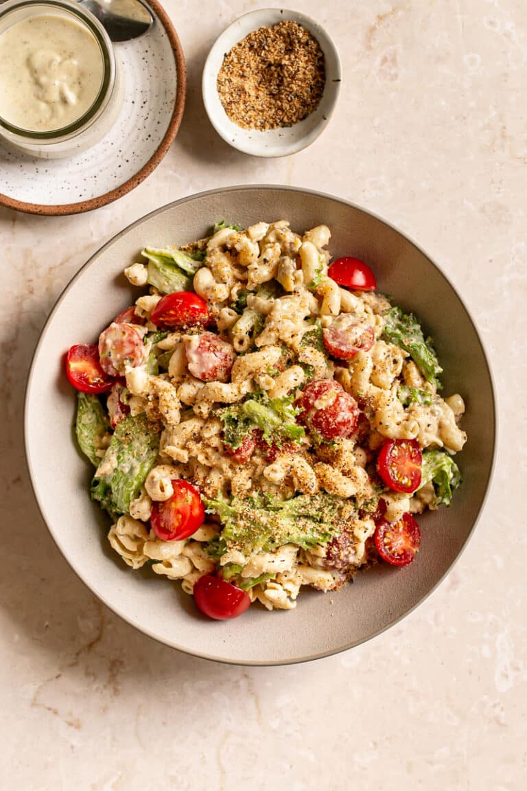 a bowl of caesar pasta salad with cherry tomatoes and lettuce, a small bowl of toasted breadcrumbs and a jar of Vegan Caesar Dressing above the salad bowl