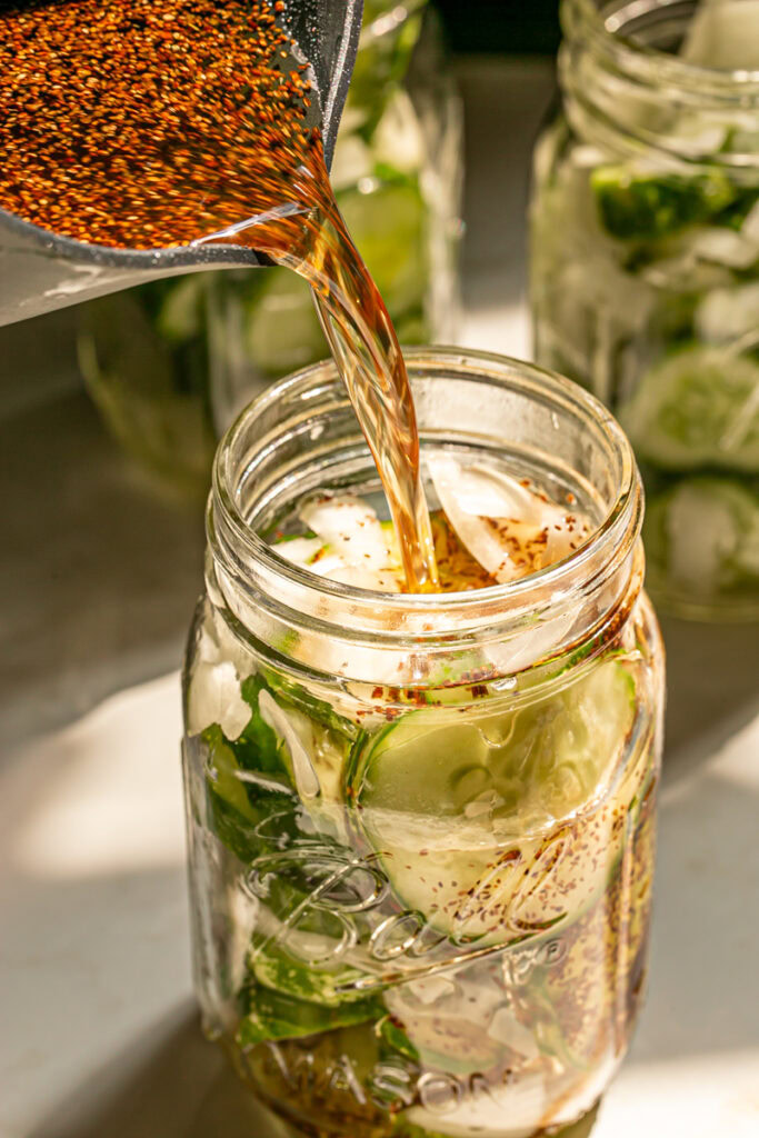 action shot of pouring the brine over the sliced cucumbers and onion in a mason jar