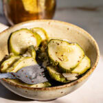 a bowl full of sliced round sweet pickles with a fork in the bowl and a jar of pickles in the background