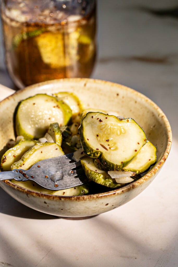 a bowl full of sliced round sweet pickles with a fork in the bowl and a jar of pickles in the background