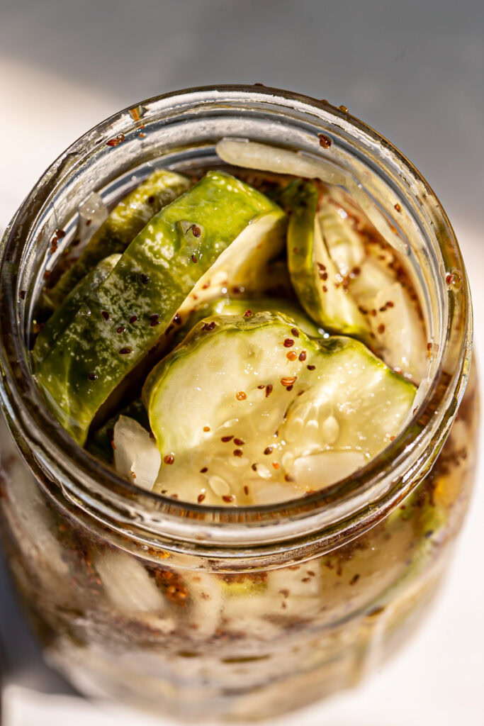 a close up of a jar of sweet pickles with the lid off to see the pickles and onion inside