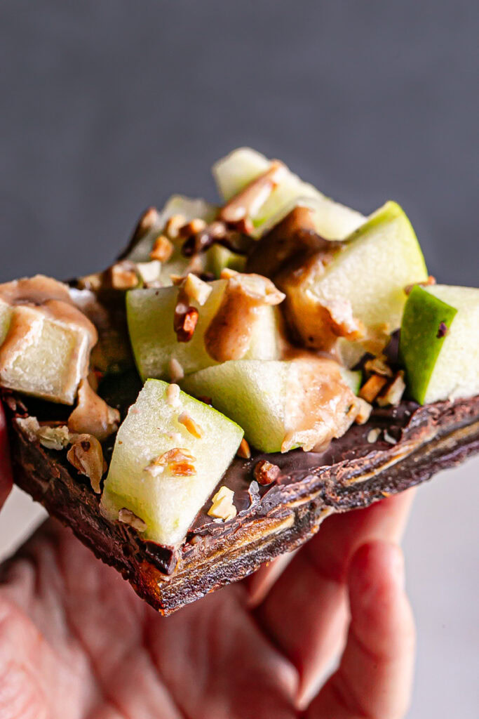 a close up of a hand holding a slice of caramel apple date bark