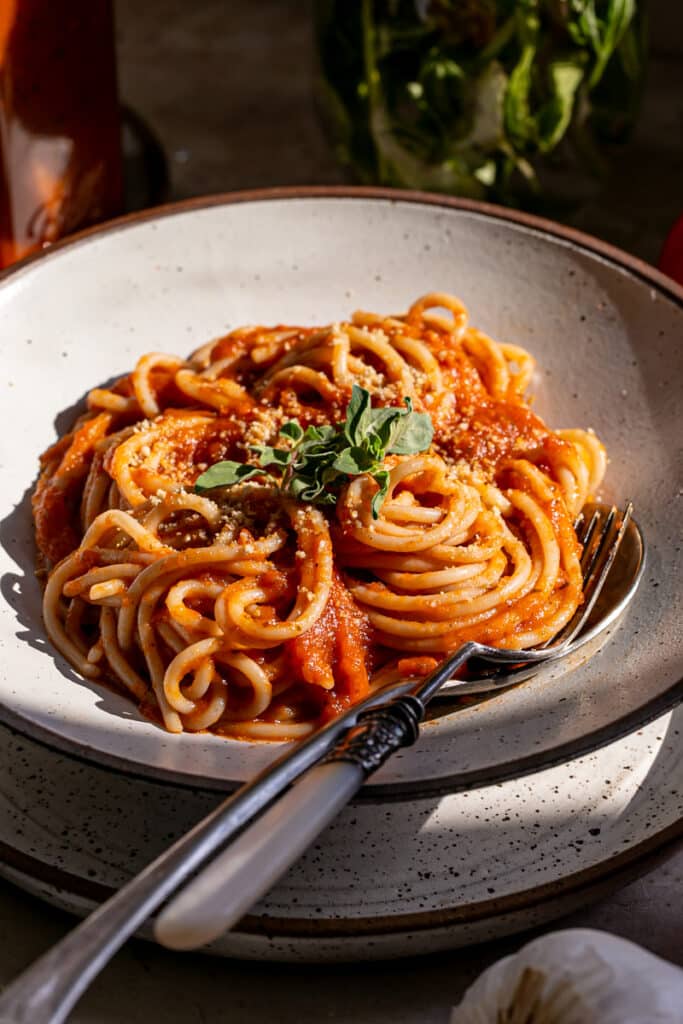 spaghetti noodles tossed in the tomato sauce in a pasta bowl with a spoon and fork