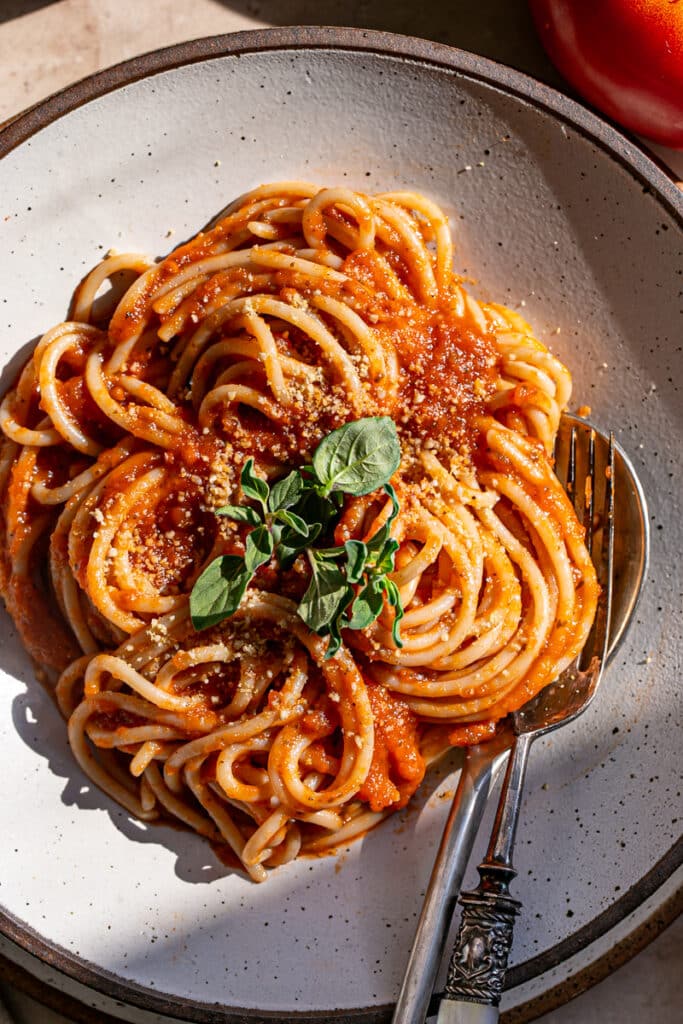 a close up of spaghetti noodles tossed in the tomato sauce in a pasta bowl with a spoon and fork
