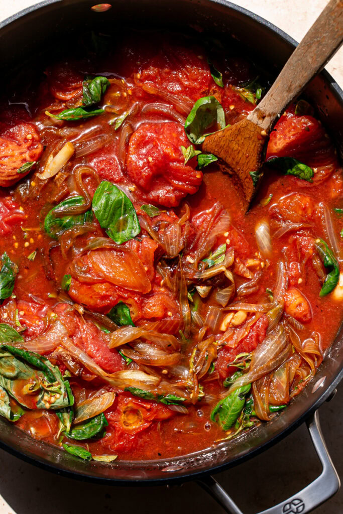 roasted tomatoes, caramelized onions, fresh basil and oregano added to a large pot stirred together with a wooden spoon in the pot