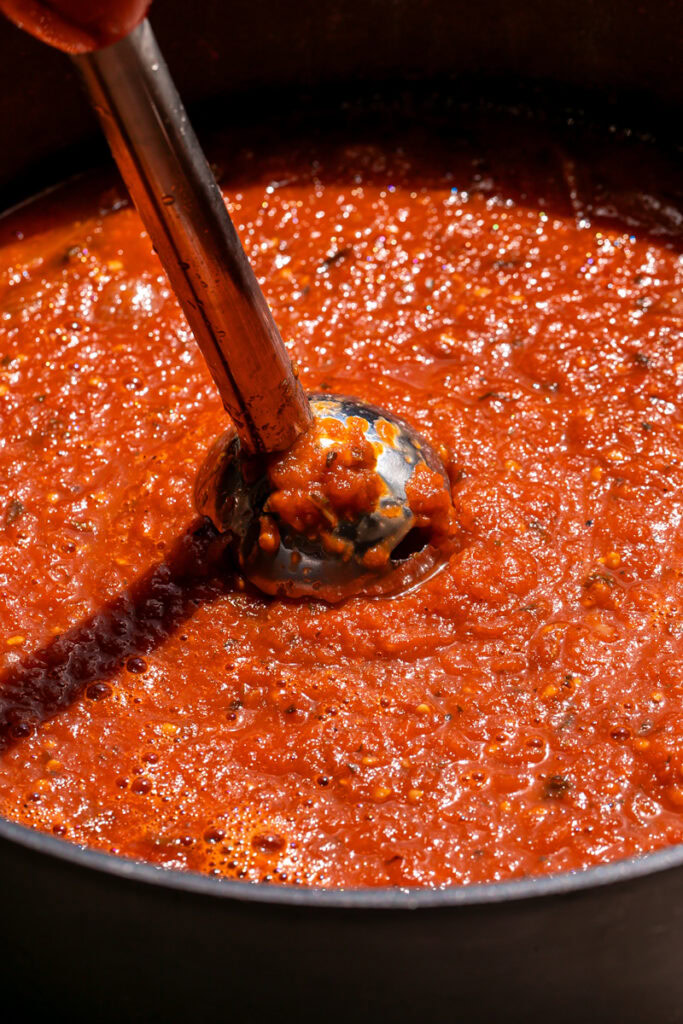 using an immersion blender to blend the tomato sauce in the pot