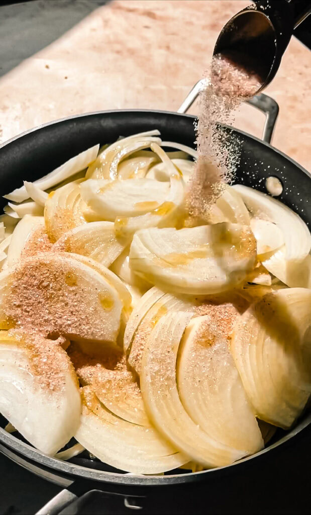 sprinkling pink Himalayan salt over sliced sweet yellow onions in a skillet